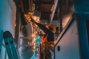 Man performing construction with a angle grinder on an air duct